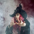 Attractive woman in witches hat with red hair performs magic. Smoke and witchcraft Royalty Free Stock Photo