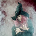 Attractive woman in witches hat with red hair performs magic. Smoke and witchcraft Royalty Free Stock Photo