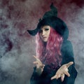 Attractive woman in witches hat with red hair performs magic. Smoke and witchcraft Royalty Free Stock Photo