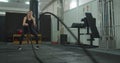 Attractive woman working out with battle ropes in the gym, intense focused woman training hard to achieve her fitness