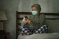 Worried middle aged woman 50s with grey hair and protective mask checking online news with mobile phone during covid-19 virus home Royalty Free Stock Photo