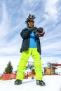 Attractive youg man tourist in funny mohawk hat, green pants, ski glasses mask and black mittens on a background of blue