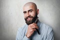 Attractive yound balded barber with thick black beard and mustache smiling while holding straight razor on his beard. A young hair