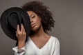 Attractive young african american woman in white shirt holding black hat over half of her face Royalty Free Stock Photo