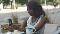 Attractive young african woman smiling and taking a selfie with her smartphone while sitting alone in outdoor cafe Royalty Free Stock Photo