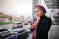 Attractive young arabian woman looks at phone haw hold in hands. Model in hijab hold on hand on chin. She stand at edge