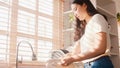 Attractive young Asia lady washing dishes while doing cleaning in the kitchen at house. Stay at home, self isolation, social Royalty Free Stock Photo