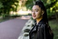 Attractive young Asian brunette woman in black leather jacket, relaxing on bench in the park outdoor. Close up of Royalty Free Stock Photo