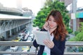 Attractive young Asian business woman talking on phone and looking document files in her hands at outside office background. Royalty Free Stock Photo