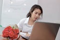 Attractive young Asian business woman working with laptop computer and a bouquet of red roses on the desk in office. Royalty Free Stock Photo