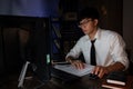 Attractive young asian businessman concentrated working until late overtime on publication at his desk in dark modern office at Royalty Free Stock Photo