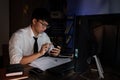 Attractive young asian businessman concentrated working until late overtime on publication at his desk in dark modern office at Royalty Free Stock Photo