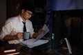 Attractive young asian businessman concentrated working until late overtime on publication at his desk in dark modern office at Royalty Free Stock Photo