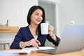 Attractive young Asian businesswoman sits at her office desk and having a hot coffee Royalty Free Stock Photo