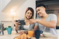 Attractive young Asian couple distracted at table with newspaper and cell phone while eating breakfast. Royalty Free Stock Photo