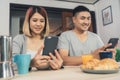 Attractive young Asian couple distracted at table with newspaper and cell phone while eating breakfast. Excited young Asian couple Royalty Free Stock Photo