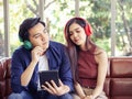 Young Asian couple sitting close together on couch ,wearing headphones  listening to music from tablet Royalty Free Stock Photo