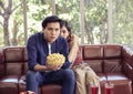 Young Asian couple sitting on couch in living room , watching scary movie,a man holding popcorn in his hand while his girlfriend Royalty Free Stock Photo