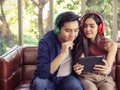 Attractive and young Asian couple sitting on couch in living room wearing headphones looking tablet and smiling Royalty Free Stock Photo