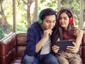 Attractive and young Asian couple sitting on couch in living room wearing headphones looking tablet and smiling Royalty Free Stock Photo