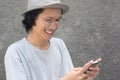 Attractive young asian man with hat and glasses using smarphone and smiling