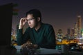 Attractive young asian man sitting on desk table looking at laptop computer in dark late night working feeling serious thinking