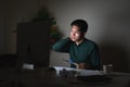 Attractive young asian man working late dark night looking at laptop computer in dark home office desk feeling tired on work load