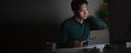 Attractive young asian man working late at night looking at laptop computer in dark home office desk feeling tired on work load or