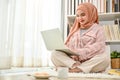 Attractive Asian Muslim female working from home, using laptop in her living room Royalty Free Stock Photo