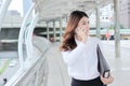Attractive young Asian secretary talking on phone and walking on walkway in city. Royalty Free Stock Photo