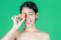 Attractive young Asian woman covering her eyes with tomato slice over green isolated background. Healthy and beauty skin care Royalty Free Stock Photo