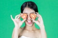 Attractive young Asian woman covering her eyes with tomato slice over green isolated background. Healthy and beauty skin care Royalty Free Stock Photo