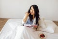 An attractive young Asian woman is lying in bed reading a book and eating berries. A charming female Korean is resting on the sofa Royalty Free Stock Photo