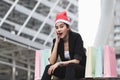 Attractive young Asian woman with santa hat and colorful shopping bag sitting outdoors after shopping for christmas gifts Royalty Free Stock Photo