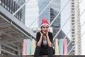 Attractive young Asian woman with santa hat and colorful shopping bag sitting outdoors after shopping for christmas gifts Royalty Free Stock Photo