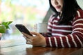 Attractive Asian woman using her smartphone while sipping coffee in the coffee shop Royalty Free Stock Photo