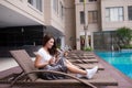 Attractive young Asian woman using tablet and drinking water near swimming pool. Relaxation concept Royalty Free Stock Photo