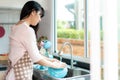 Attractive young Asian woman is washing dishes at kitchen sink while doing cleaning at home during Staying at home using free time Royalty Free Stock Photo