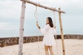 Attractive young asian woman in white dress playing a wooden swing on the beach in summer Royalty Free Stock Photo