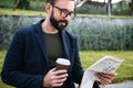 Attractive young bearded man sitting outdoors reading newspaper Royalty Free Stock Photo