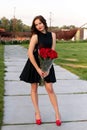 Attractive young birthday girl with brown hair in little black dress posing, smiling and holding a bouquet of red roses Royalty Free Stock Photo