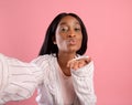 Attractive young black woman taking selfie, blowing air kiss on pink studio background Royalty Free Stock Photo