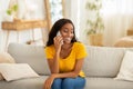 Attractive young black woman talking on mobile phone and smiling while sitting on sofa at home Royalty Free Stock Photo