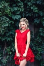 Attractive young blonde girl in red dress posing near a wild vineyard. Royalty Free Stock Photo