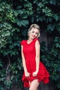 Attractive young blonde girl in red dress posing near a wild vineyard. Royalty Free Stock Photo