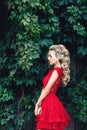 Attractive young blonde girl in red dress posing near a wild vineyard. Royalty Free Stock Photo