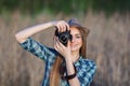 Attractive young blonde woman in blue plaid shirt straw hat enjoying her time taking photos on meadow outdoors Royalty Free Stock Photo