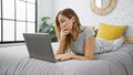 Attractive young blonde woman is comfortably lying in bed and using her laptop to hop online in a cozy home ambiance with a Royalty Free Stock Photo