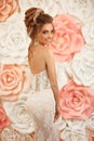 Attractive young bride with makeup and hairstyle, in wedding dress. Closeup portrait of young gorgeous woman over roses wall Royalty Free Stock Photo