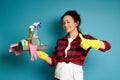 Attractive curly woman wearing yellow rubber gloves holds cleaning supplies in one hand and shows a thumb up to camera standing on Royalty Free Stock Photo